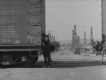 Movie still from “Sherlock Jr.” (1924), directed by Buster Keaton – A man standing next to a train car on the side of the road; Extreme Wide shot, Low angle