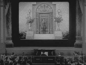 Movie still from “Sherlock Jr.” (1924), directed by Buster Keaton – An old photo of an orchestra performing in front of an audience; Extreme Wide shot, Low angle