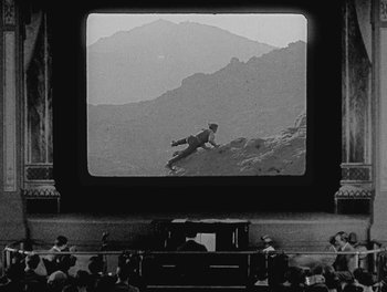 Movie still from “Sherlock Jr.” (1924), directed by Buster Keaton – A man riding a skate board on top of a hill; Extreme Wide shot, High angle