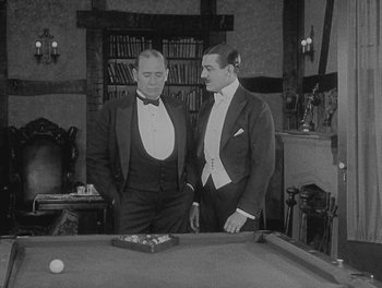Movie still from “Sherlock Jr.” (1924), directed by Buster Keaton – Two men standing next to a pool table in a room; Medium shot, High angle