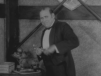 Movie still from “Sherlock Jr.” (1924), directed by Buster Keaton – An old photo of a man in a tuxedo holding a knife; Medium shot, Low angle