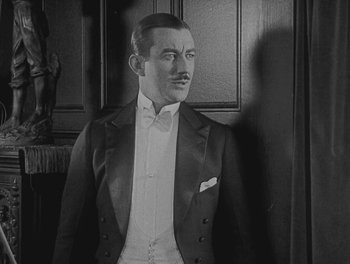 Movie still from “Sherlock Jr.” (1924), directed by Buster Keaton – A man wearing a suit and a bow tie standing in front of a wall; Medium shot, High angle