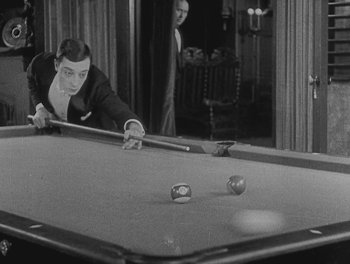 Movie still from “Sherlock Jr.” (1924), directed by Buster Keaton – A black and white photo of a man playing a game of billiards; Medium shot, High angle