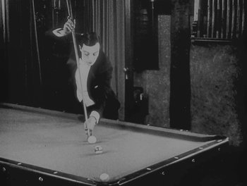 Movie still from “Sherlock Jr.” (1924), directed by Buster Keaton – A man in a black suit playing a game of billiards; Medium shot, High angle