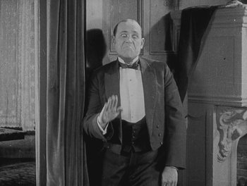 Movie still from “Sherlock Jr.” (1924), directed by Buster Keaton – An old photo of a man in a suit and bow tie; Medium shot, Low angle