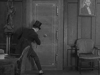 Movie still from “Sherlock Jr.” (1924), directed by Buster Keaton – A man in a suit and top hat in front of an open door; Wide shot, High angle