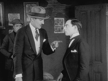 Movie still from “Sherlock Jr.” (1924), directed by Buster Keaton – Two men in suits and hats talking to each other; Medium shot, Over the shoulder angle