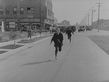 Movie still from “Sherlock Jr.” (1924), directed by Buster Keaton – Black and white photograph of men running down a street; Wide shot, High angle