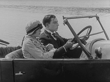 Movie still from “Sherlock Jr.” (1924), directed by Buster Keaton – A man and a woman driving a car on a river; Medium shot, High angle