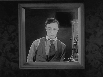 Movie still from “Sherlock Jr.” (1924), directed by Buster Keaton – A black and white photo of a man looking at himself in a mirror; Medium shot, Low angle