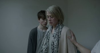 Movie still from “22 July” (2018), directed by Paul Greengrass – A woman standing next to a young boy in front of a white wall; Medium shot, Over the shoulder angle