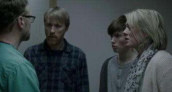 Movie still from “22 July” (2018), directed by Paul Greengrass – A man and a woman and a boy standing next to each other in a room; Medium shot, Over the shoulder angle