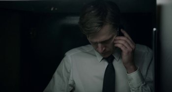Movie still from “22 July” (2018), directed by Paul Greengrass – A man wearing a white shirt and a black neck tie talking on a cell phone; Close Up shot, Low angle