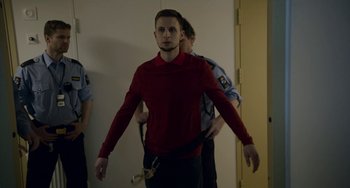 Movie still from “22 July” (2018), directed by Paul Greengrass – A man in a red shirt is being escorted by police officers; Medium shot, Low angle