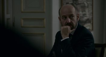 Movie still from “22 July” (2018), directed by Paul Greengrass – A man in a suit and tie sitting in front of a door; Close Up shot, Over the shoulder angle