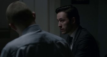 Movie still from “22 July” (2018), directed by Paul Greengrass – A man wearing a suit and tie sitting in front of another man; Close Up shot, Over the shoulder angle