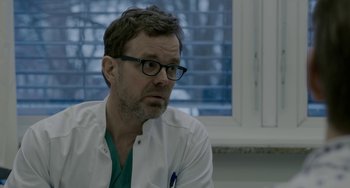 Movie still from “22 July” (2018), directed by Paul Greengrass – A man wearing glasses and a white lab coat; Close Up shot, Over the shoulder angle