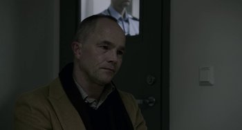Movie still from “22 July” (2018), directed by Paul Greengrass – A man sitting in front of a door looking into the distance; Medium shot, Over the shoulder angle
