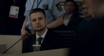 Movie still from “22 July” (2018), directed by Paul Greengrass – A man in a suit sitting in front of a group of people; Close Up shot, Over the shoulder angle