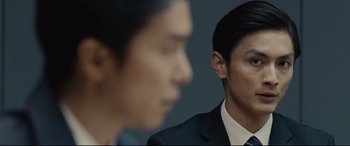 Movie still from “Shin Godzilla” (2016), directed by Shinji Higuchi – A man in a black suit and a man in a black suit; Close Up shot, Over the shoulder angle