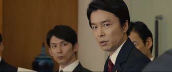 Movie still from “Shin Godzilla” (2016), directed by Shinji Higuchi – Two men in suits and ties standing next to each other; Close Up shot, Over the shoulder angle