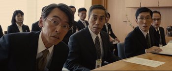 Movie still from “Shin Godzilla” (2016), directed by Shinji Higuchi – A group of men in suits and ties sitting at a table; Medium shot, Low angle