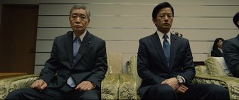 Movie still from “Shin Godzilla” (2016), directed by Shinji Higuchi – Two men in business suits sitting on a couch; Medium shot, Low angle
