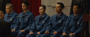 Movie still from “Shin Godzilla” (2016), directed by Shinji Higuchi – A group of men sitting next to each other in blue uniforms; Medium shot, Low angle