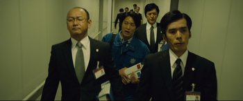 Movie still from “Shin Godzilla” (2016), directed by Shinji Higuchi – A group of men in suits walking down a hallway; Medium shot, Low angle