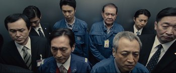 Movie still from “Shin Godzilla” (2016), directed by Shinji Higuchi – A group of men standing next to each other in an elevator; Medium shot, Low angle
