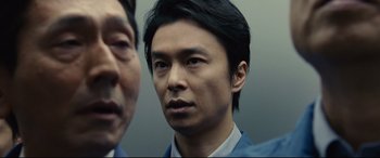 Movie still from “Shin Godzilla” (2016), directed by Shinji Higuchi – A person wearing a suit; Close Up shot, Low angle