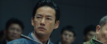 Movie still from “Shin Godzilla” (2016), directed by Shinji Higuchi – A person wearing glasses and a suit; Close Up shot, Over the shoulder angle