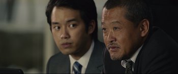 Movie still from “Shin Godzilla” (2016), directed by Shinji Higuchi – Two men in business suits sitting next to each other; Close Up shot, Over the shoulder angle