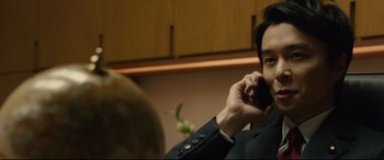 Movie still from “Shin Godzilla” (2016), directed by Shinji Higuchi – A man talking on a cell phone while sitting in a room; Close Up shot, Low angle