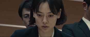 Movie still from “Shin Godzilla” (2016), directed by Shinji Higuchi – A young woman with short black hair wearing a black suit; Close Up shot, Over the shoulder angle