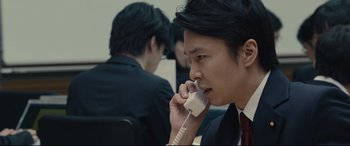 Movie still from “Shin Godzilla” (2016), directed by Shinji Higuchi – A man in a business suit talking on a phone; Close Up shot, Low angle