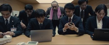 Movie still from “Shin Godzilla” (2016), directed by Shinji Higuchi – A group of men sitting around a table looking at a laptop; Medium shot, Low angle