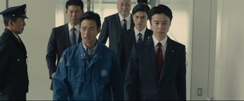 Movie still from “Shin Godzilla” (2016), directed by Shinji Higuchi – A group of men in suits and ties standing next to each other; Medium shot, Low angle