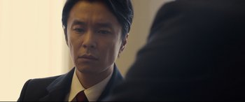 Movie still from “Shin Godzilla” (2016), directed by Shinji Higuchi – A person wearing a suit and tie; Close Up shot, Over the shoulder angle