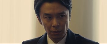 Movie still from “Shin Godzilla” (2016), directed by Shinji Higuchi – A person wearing a suit and tie; Close Up shot, Low angle