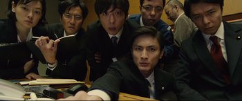 Movie still from “Shin Godzilla” (2016), directed by Shinji Higuchi – A group of men in suits and ties in a room; Medium shot, Low angle