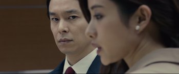 Movie still from “Shin Godzilla” (2016), directed by Shinji Higuchi – A man and a woman in business attire looking at the camera; Close Up shot, Over the shoulder angle