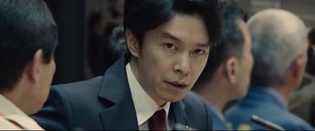 Movie still from “Shin Godzilla” (2016), directed by Shinji Higuchi – A man wearing a suit and tie looking at the camera; Close Up shot, Low angle
