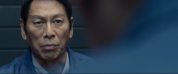 Movie still from “Shin Godzilla” (2016), directed by Shinji Higuchi – An older asian man looking at the camera; Close Up shot, Over the shoulder angle