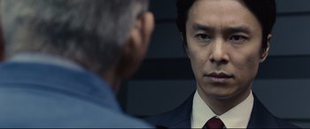 Movie still from “Shin Godzilla” (2016), directed by Shinji Higuchi – A person wearing a suit and tie; Close Up shot, Over the shoulder angle