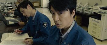 Movie still from “Shin Godzilla” (2016), directed by Shinji Higuchi – A man in a blue jacket is looking at the camera; Close Up shot, Low angle