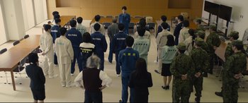 Movie still from “Shin Godzilla” (2016), directed by Shinji Higuchi – A group of people standing in front of an instructor; Wide shot, High angle