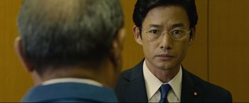 Movie still from “Shin Godzilla” (2016), directed by Shinji Higuchi – A man in a suit and tie looking at another man in a suit and tie; Close Up shot, Over the shoulder angle