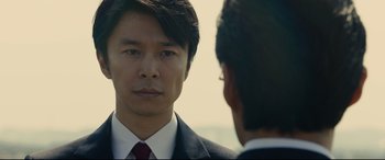 Movie still from “Shin Godzilla” (2016), directed by Shinji Higuchi – A man in a suit and tie looking at another man in a suit and tie; Close Up shot, Over the shoulder angle