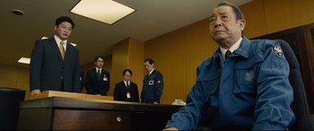 Movie still from “Shin Godzilla” (2016), directed by Shinji Higuchi – A group of men standing around a table; Medium shot, Low angle
